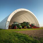 Farm tractors and harvesting equipment stored inside a large fabric hoop building for weather protection and secure agricultural storage.